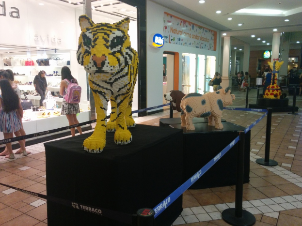 Statuen von Tieren auf schwarzen Kisten umgeben von Pfählen mit Gummibändern, mit Geschäften, die Taschen, Schuhe und andere Gegenstände ausstellen, und Menschen, die herumlaufen.