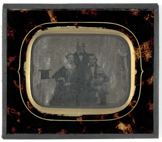 Schwarz-weißes foto eines mans in einem anzug und einer krawatte und einer frau in einem unbekannten outfit, die vor einem fernseher stehen, beide mit ernsten ausdrucken.