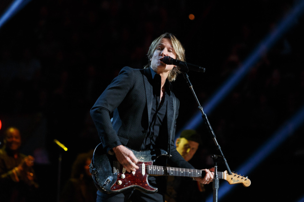 Keith Urban performs auf der Bühne im Joint in Las Vegas und spielt eine Gitarre mit einem Mikrofon davor und Musikern im Hintergrund bei dunkler Beleuchtung.