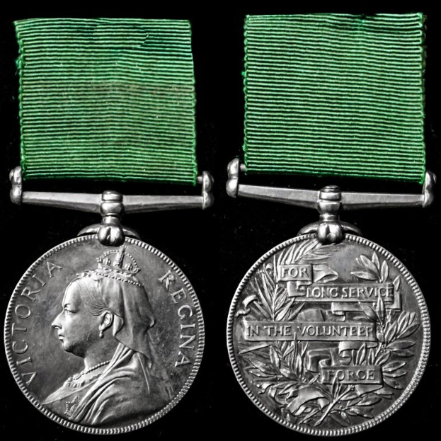 Zwei silberne Medaillen mit grünen Bändern, eine mit einem Personenbildnis und die andere mit eingravierter Schrift, vor schwarzem Hintergrund, wahrscheinlich aus dem Dienst in der Freiwilligen Feuerwehr.