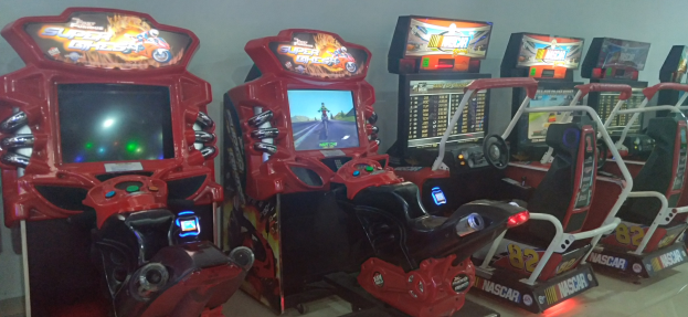 Reihe bunter Arcade-Rennwagen-Maschinen auf einem gefliesten Boden vor einer Wand.