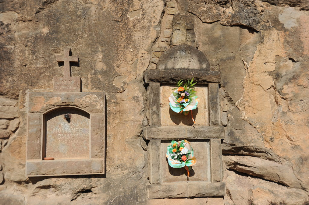 Gedenktafeln in eine Wand eingelassen mit Blumensträußen davor.