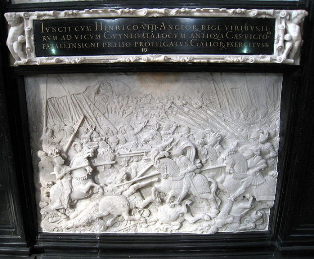 Weißer Marmorplakette mit schwarzem Rahmen, der eine Relief-Schlachtsszene zeigt, mit bewaffneten Figuren und Zuschauern drumherum.