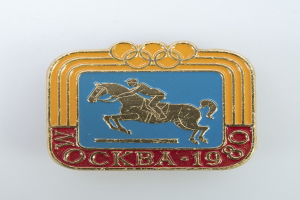 Olympische Spiele-Badge von den Olympischen Winterspielen 1988 mit einer Person in weißem Hemd und blauen Shorts auf einem rotbraunen Pferd mit weißer Mähne und Schweif vor einem hellblauen Himmel mit weißen Wolken.