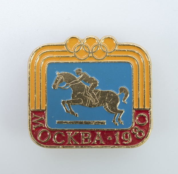 Olympische Spiele-Badge von den Olympischen Winterspielen 1988 mit einer Person in weißem Hemd und blauen Shorts auf einem rotbraunen Pferd mit weißer Mähne und Schweif vor einem hellblauen Himmel mit weißen Wolken.