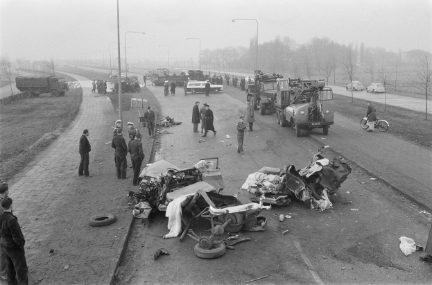 Schwarze und weiße Szenerie eines Autounfalls am Straßenrand mit mehreren Fahrzeugen, einer Gruppe von Menschen in der Nähe, Laternen, Bäumen und dem Himmel im Hintergrund.