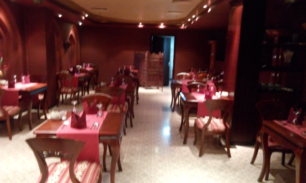 Ein Restaurantinnenraum mit Tischen und Stühlen, die mit Besteck, Servietten und Blumenvasen gedeckt sind, Wände mit Lichtern geschmückt, die eine gemütliche Atmosphäre schaffen.