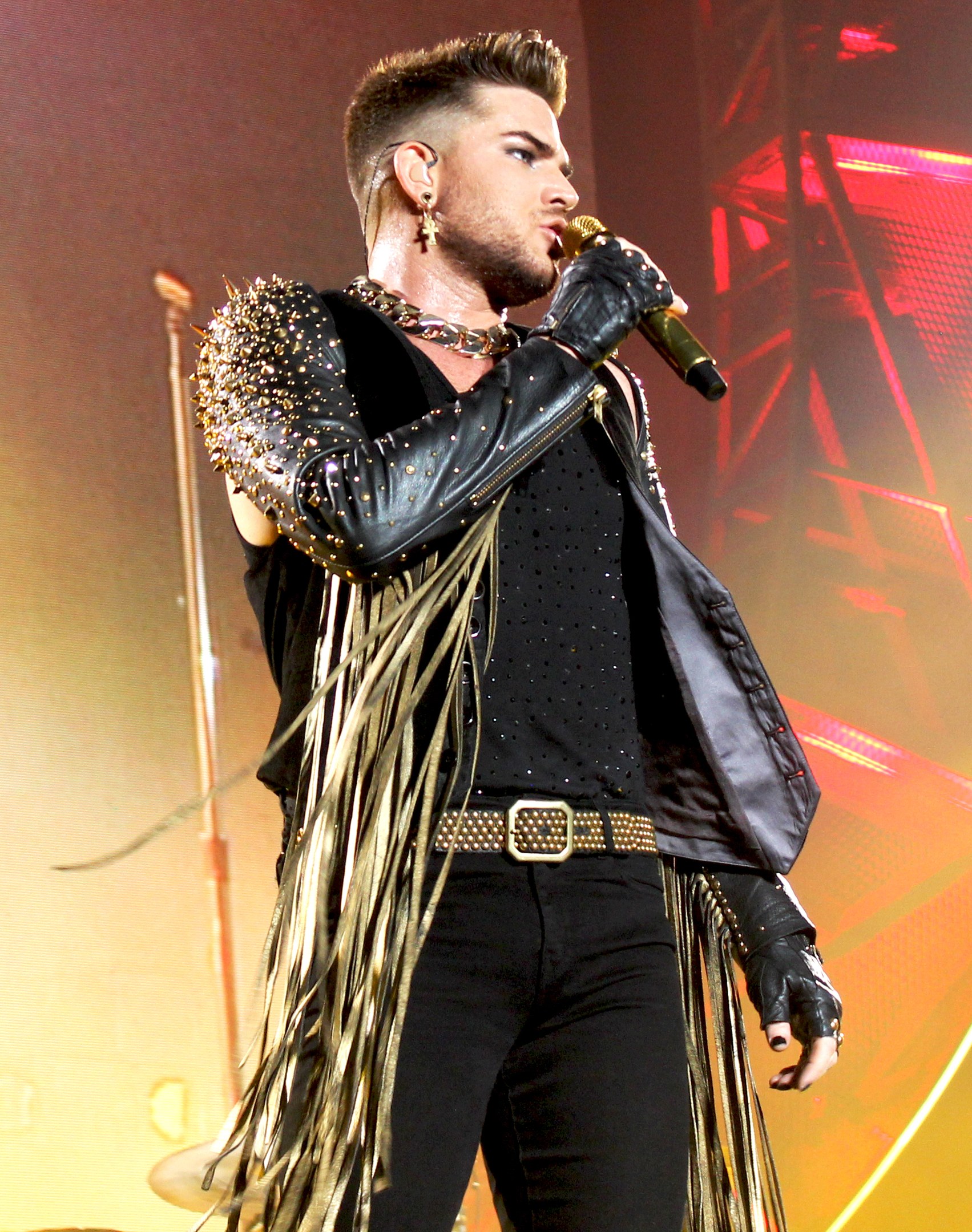 Adam Lambert performs in einem schwarzen Kleid auf der Bühne der O2 Arena in London und hält ein Mikrofon in der Hand.