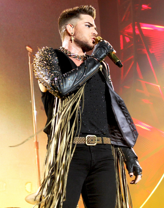 Adam Lambert performs in einem schwarzen Kleid auf der Bühne der O2 Arena in London und hält ein Mikrofon in der Hand.