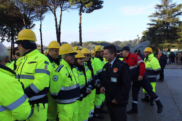 Gruppe von Notfallhelfern in gelben Westen und Helmen auf einer Straße mit Bäumen und einem klaren blauen Himmel im Hintergrund.