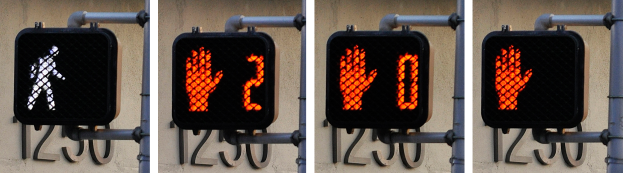 Eine Ampel mit drei Signalen an einem Gebäude befestigt, mit einer Wand im Hintergrund.