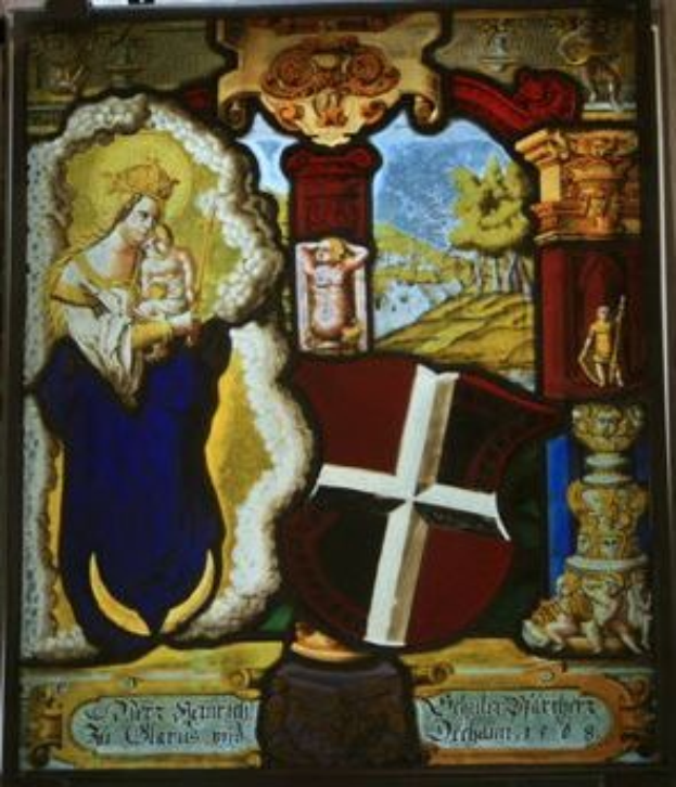 Ein Kirchenfenster aus Buntglas, das die Jungfrau Maria in einem weißen Kleid und einem Heiligenschein zeigt, die ein Baby hält, umgeben von einem Kreuz, einem Schild und einer Krone, mit religiöser Schrift in Schrifttyp.