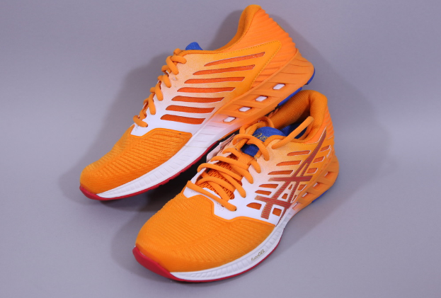 Ein Paar Asics Gel-Nimbus 22 Laufschuhe in Orange, Weiß und Blau, das auf einer grauen Oberfläche platziert ist und ein Mesh-Obermaterial, eine gepolsterte Zwischensohle und eine strapazierfähige Außensohle aufweist.