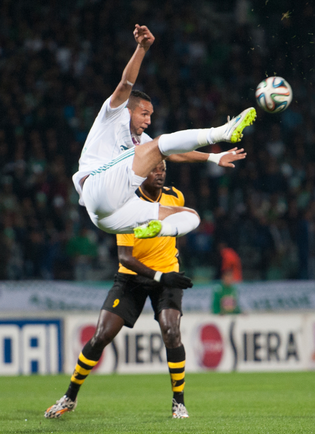 Zwei Männer spielen Fußball mit einem Banner im Hintergrund.