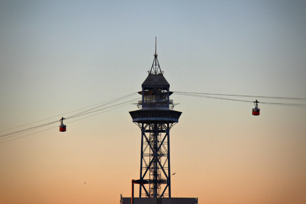 Ein paar Kabelbahnen, die an Seilen hängen, mit einem Turm im Hintergrund.