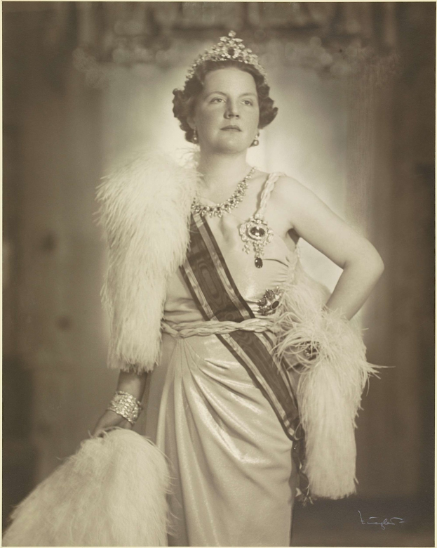 Schwarz-weiß-Foto der Queen Elizabeth II in einem Kleid und einer Krone mit unscharfem Hintergrund und Text unten.