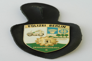 Ein schildförmiges Polizeibadgebnis mit "Polizei Berlin" in fetter schwarzer Schrift auf einem blauen Hintergrund mit einem weißen Stern und Rahmen, das auf einer Oberfläche ruht.