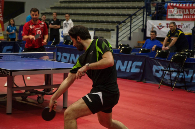 Gruppe von Menschen in legerer Kleidung, die auf einem Tisch in der Nähe einer Treppe mit Stühlen im Hintergrund ein Ballspiel spielen.
