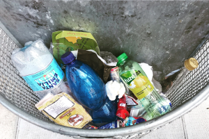 Metallmülltonne mit verschiedenen Plastikflaschen, Tüten und anderen Abfällen.