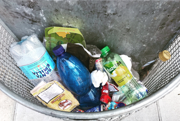 Metallmülltonne mit verschiedenen Plastikflaschen, Tüten und anderen Abfällen.