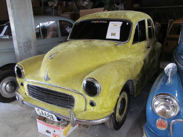 Eine Reihe von Oldtimern, die vor einer Wand mit verschiedenen Zubehörteilen geparkt sind, mit einer Säule auf der linken Seite.