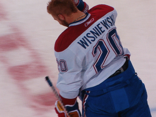 Ein Hockey-Spieler in einem 'Wisniewski'-Trikot steht auf dem Eis und hält einen Hockey-Schläger in der Hand.