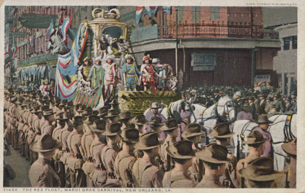 Eine alte Postkarte, die einen Mardi Gras-Umzug in New Orleans zeigt, mit einem Float, der mit Flaggen und Gegenständen geschmückt ist, Menschen auf Pferden und Zuschauern am Straßenrand, im Hintergrund Gebäude mit Fenstern und Geländern, und der Text "The Rex Float, Mardi Gras Carnival, New Orleans" unten.