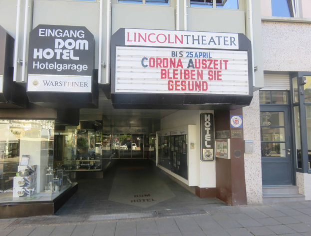 Außenansicht des Lincoln Theaters in Berlin, Deutschland, mit Glasfenstern und -türen sowie einer Tafel und einem Innenblick, der eine belebte Stadtlandschaft mit verschiedenen Gegenständen zeigt.