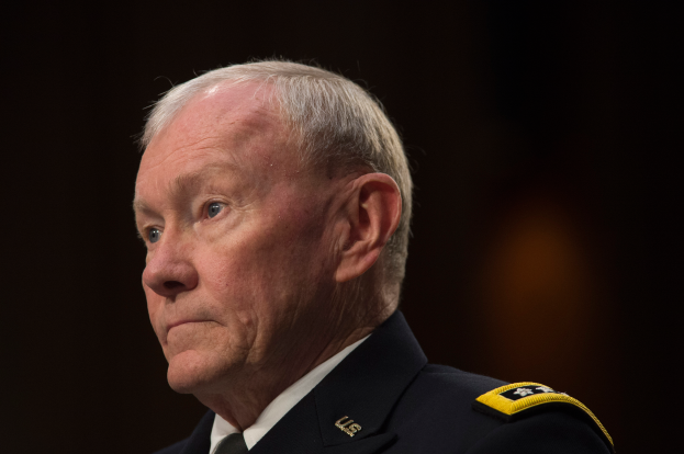 Mann in militärischer Uniform sitzt an einem Tisch mit dunklem Hintergrund, als Verteidigungsminister identifiziert.