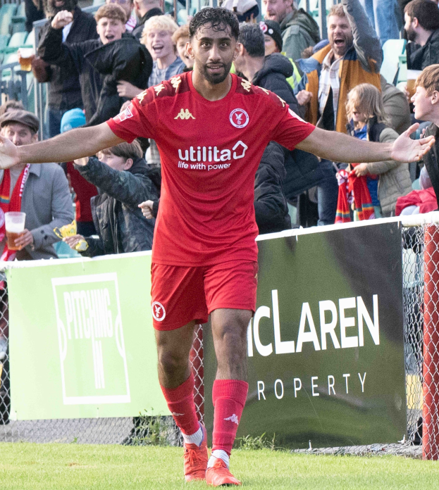 Ein Fussballspieler in roter Uniform rennt auf einem Feld mit ausgestreckten Armen, umgeben von Zuschauern hinter einem Zaun, mit einem "Middlesbrough FC v Swansea City - Sky Bet Championship"-Schild im Hintergrund.