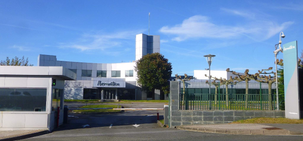 Ein großes, mehrfenstriges Gebäude mit einem Tor davor, umgeben von Straßenlaternen, Lampen, Gittern, Bäumen, Gras und einem bewölkten Himmel, das als Hauptsitz von Iberostica in den Niederlanden dient.