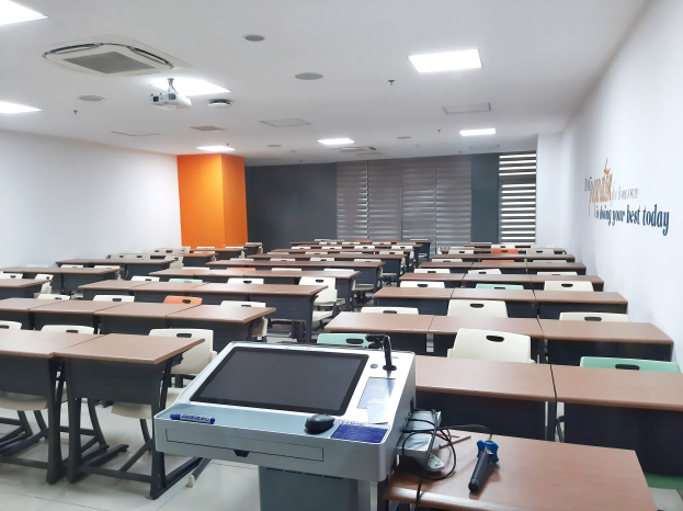 Ein Klassenzimmer mit Tischen, Stühlen, einem Deckenprojektor und Gegenständen auf den Tischen, mit Text an der rechten Wand, der darauf hinweist, dass es sich um eine Privatschule in Singapur handelt.