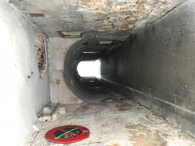 Ein Tunnel mit einem roten und schwarzen "Zutritt verboten"-Schild auf dem Boden, beleuchtet von Deckenlampen, das darauf hinweist, dass es Teil eines Abwassersystems ist.