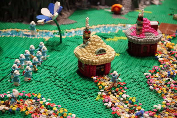 Ein Lego-Modell einer Kleinstadt mit Häusern, Blumen, Pflanzen und Spielzeugen, mit einem unscharfen Hintergrund, der einen träumerischen Effekt erzeugt.