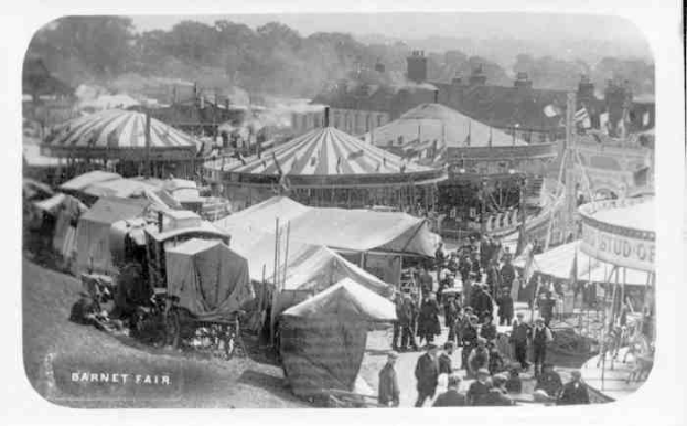 Ein altes Schwarz-Weiß-Foto einer belebten KarnevalsSzene mit Zelten, Menschen, Karren, Pfählen, Bäumen und Gebäuden im Hintergrund, mit der Aufschrift "Barnet Fair, London, England" unten.