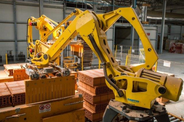 Großes Industriegebäude mit gestapelten Kisten, Kranen, Zaun, Strommasten und einer fernen Wand in einer Fertigungseinrichtung.