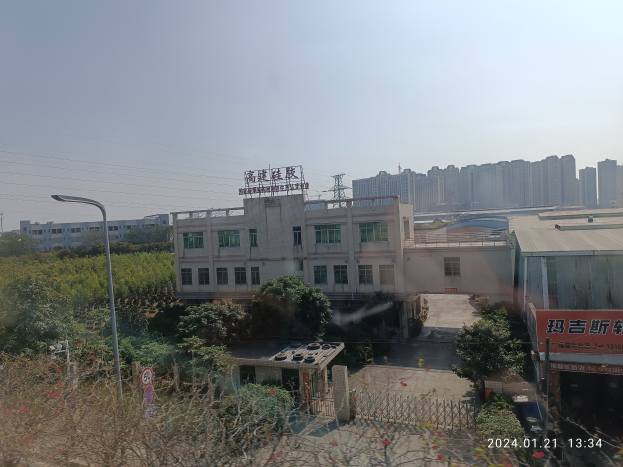 Eine Stadtansicht von einem Gebäude aus, mit verschiedenen Gebäuden, Grünflächen, Straßeninfrastruktur, Fahrzeugen und einer Fabrik mit einem Schild "Zhejiang Zhongshan Automotive Machinery Co., Ltd." unter einem klaren blauen Himmel.
