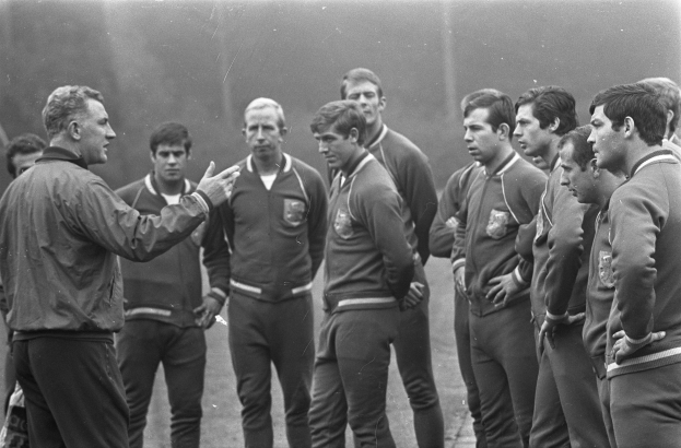 Ein Schwarz-Weiß-Foto einer Gruppe von Männern auf einem Fußballfeld, wobei der Mann in der Mitte einen Wanderstiefel trägt.