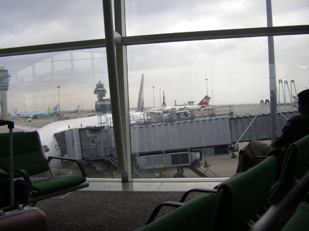 Ein Bild von hinter einem Fenster, das mehrere Stühle, einen Koffer auf der linken Seite, Flugzeuge und andere Abteile zeigt.