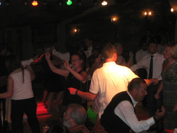 Lebendige Partyszene mit tanzenden Menschen auf der Tanzfläche unter verschiedenen farbigen Lichtern in einem dunklen Raum.