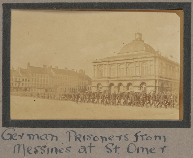 Deutsche Kriegsgefangene aus Messines vor einem Gebäude mit einem klaren blauen Himmel im Hintergrund, Text unten sichtbar.