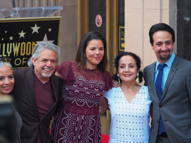 Gruppe von Menschen auf einem roten Teppich bei der Zeremonie der Hollywood Walk of Fame mit einer Tafel, einem Glastisch und einer Wand im Hintergrund.