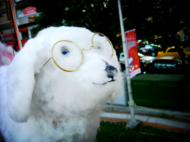 Eine hündchenförmige Puppe vorne mit Fahrzeugen, Bäumen und Gebäuden im Hintergrund und einer Fahne in der Mitte.