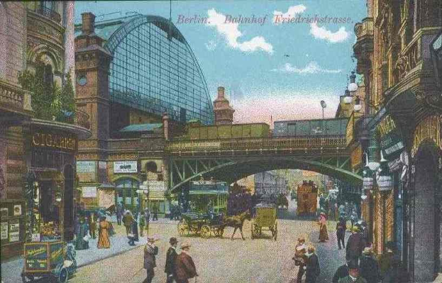 Alte Postkarte zeigt eine belebte Berliner Stadtstraße mit Fußgängern, Pferdewagen, Gebäuden, Laternen, einer Brücke und einem bewölkten Himmel, mit Text oben.