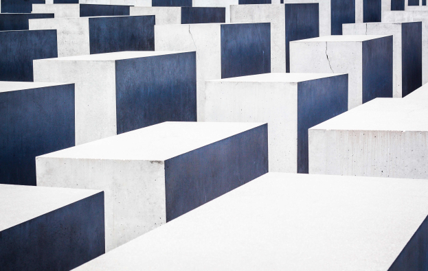 Eine große Anzahl rechteckiger Betonplatten in verschiedenen Höhen, die in einem Gittermuster auf einem geneigten Feld angeordnet sind, mit einer ernsten Atmosphäre.