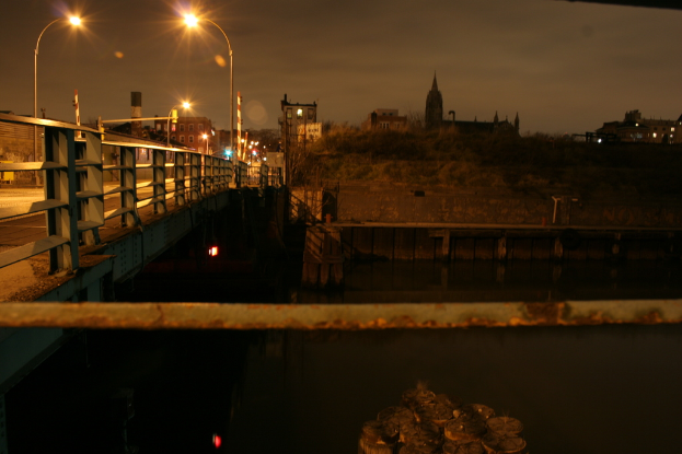 Eine Brücke überspannt einen Fluss mit mehreren Straßenlaternen darauf und zahlreichen Gebäuden im Hintergrund.